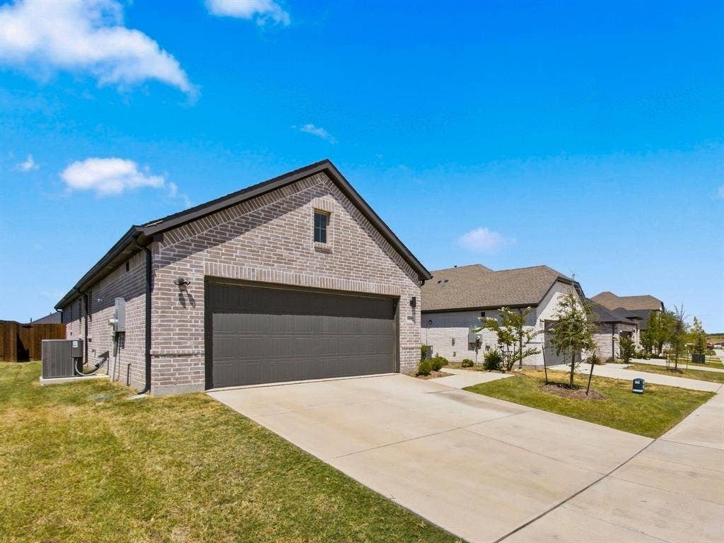 1157 Butterfly Dale Drive, Lavon, TX 75166 Brick exterior featuring a gabled roofline, a two-car garage with a paneled door, and a concrete driveway