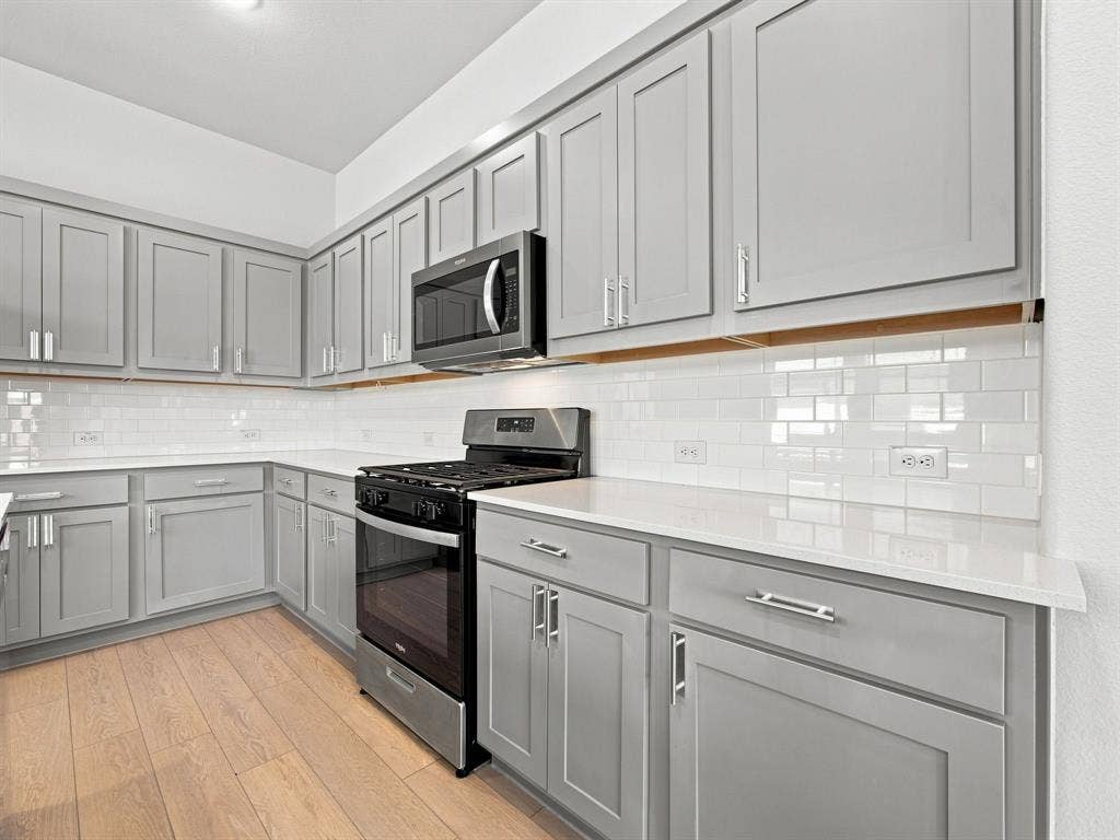 1157 Butterfly Dale Drive, Lavon, TX 75166 Kitchen featuring shaker-style grey cabinetry, white solid-surface countertops, white subway tile backsplash, wood-finish flooring, and stainless steel appliances