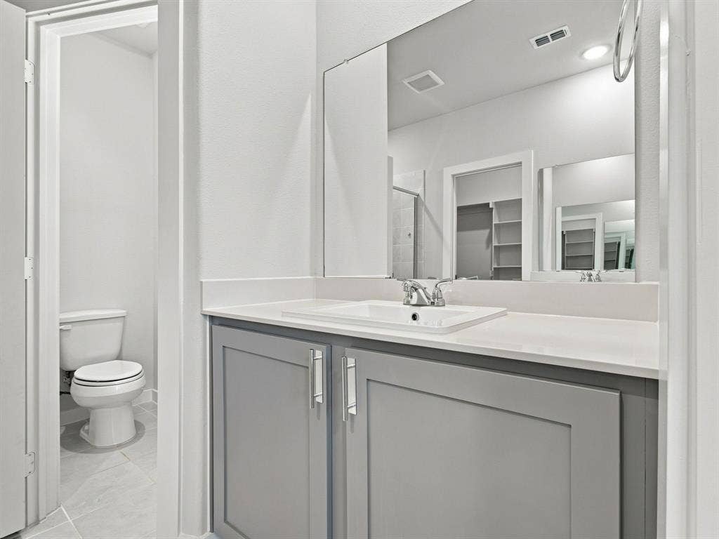 1157 Butterfly Dale Drive, Lavon, TX 75166 Bathroom vanity featuring a grey shaker-style cabinet, white solid-surface countertop, integrated rectangular sink, polished chrome faucet, and expansive wall-mounted mirror
