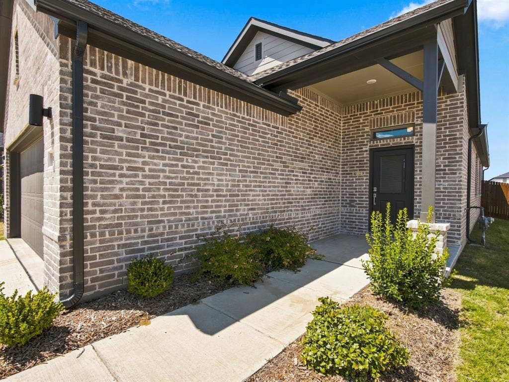 1157 Butterfly Dale Drive, Lavon, TX 75166 Brick exterior featuring a covered front porch, dark-toned trim, concrete walkway, and recessed entry lighting