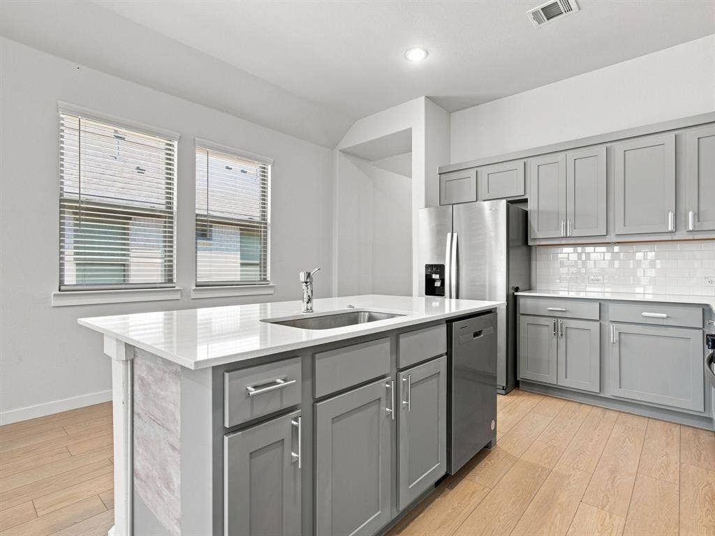 1157 Butterfly Dale Drive, Lavon, TX 75166 Kitchen featuring grey cabinetry, white countertops, a central island with a stainless steel undermount sink, subway tile backsplash, and light-toned wood-finish flooring