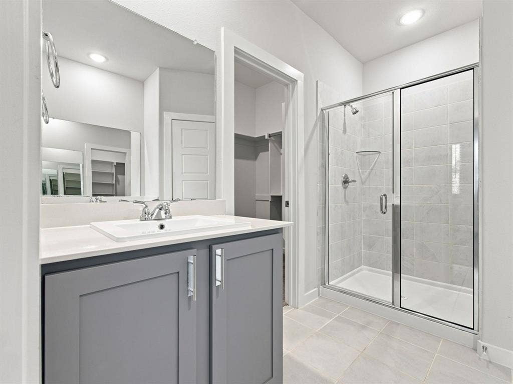 1157 Butterfly Dale Drive, Lavon, TX 75166 Grey cabinetry with silver-tone hardware, rectangular undermount sink, quartz countertop, large wall-mounted mirror, and glass-enclosed shower with tiled surround