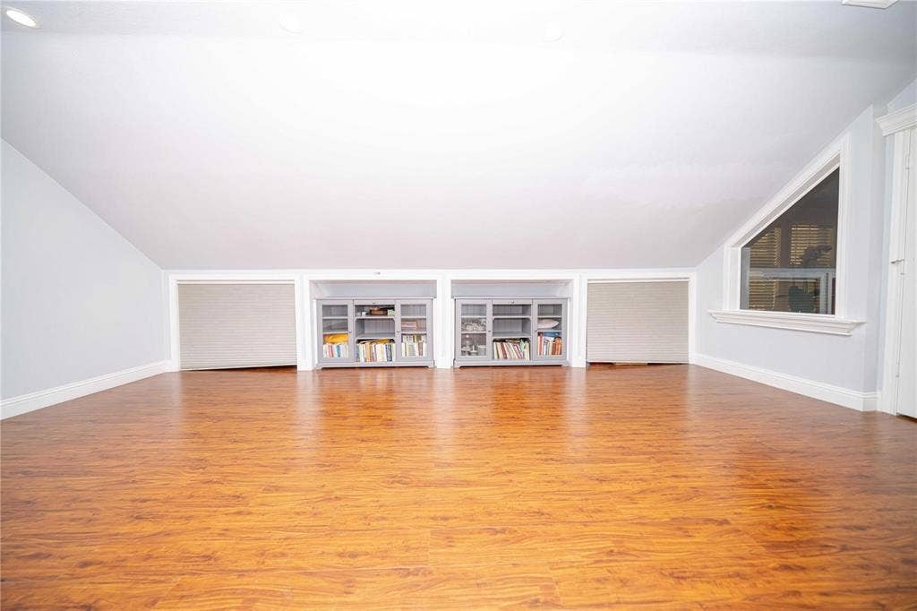 Sloped ceiling featuring recessed lighting, wood-finish flooring, built-in cabinetry with glass-front doors, and a triangular window