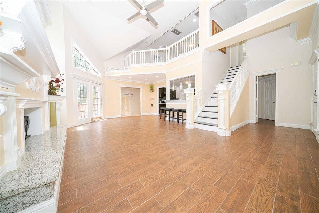Two-story living area featuring vaulted ceilings, wood-finish flooring, a stone-surround fireplace, a mezzanine overlook with white railing, and a staircase with decorative millwork