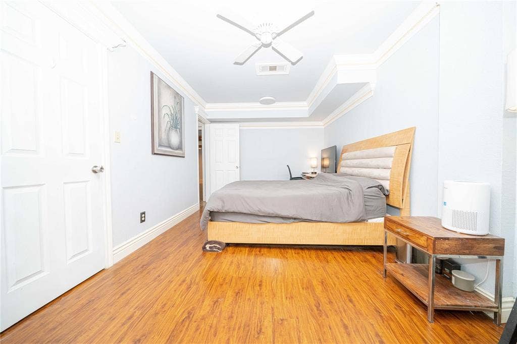 Room featuring wood-finish flooring, recessed tray ceiling, crown molding, and a central ceiling fan
