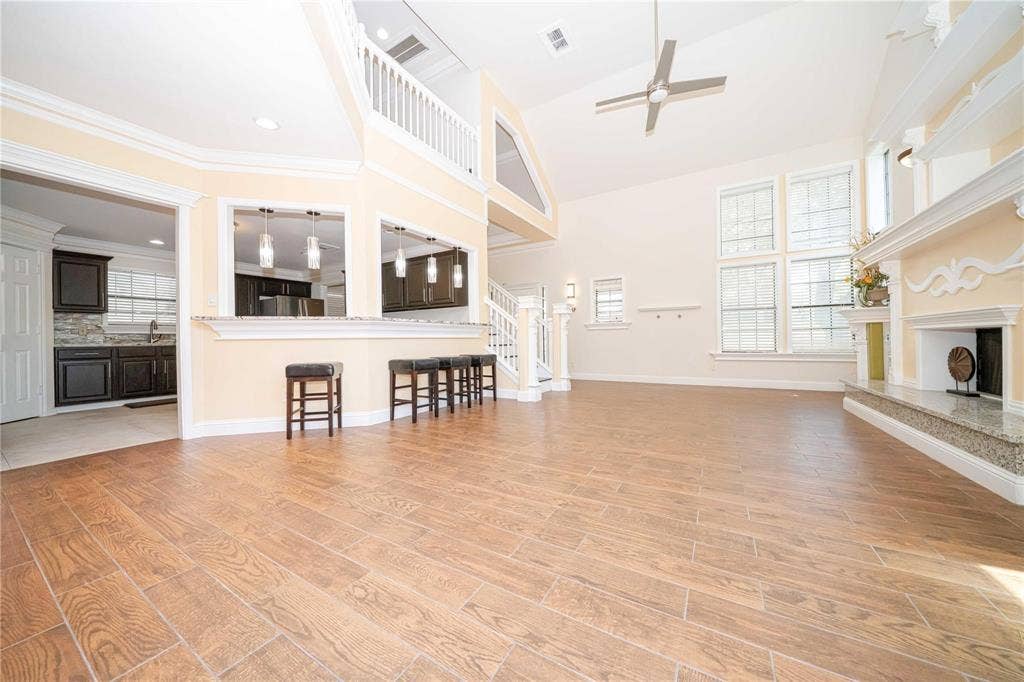 Open-concept living area featuring vaulted ceilings, wood-finish flooring, a stone-surround fireplace with a mantel, and multi-pane windows