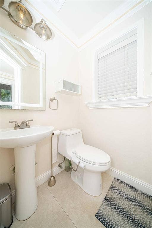 Pedestal sink with dual-handle polished chrome faucet, wall-mounted light fixture, single-piece elongated toilet, built-in shelving, and tile flooring