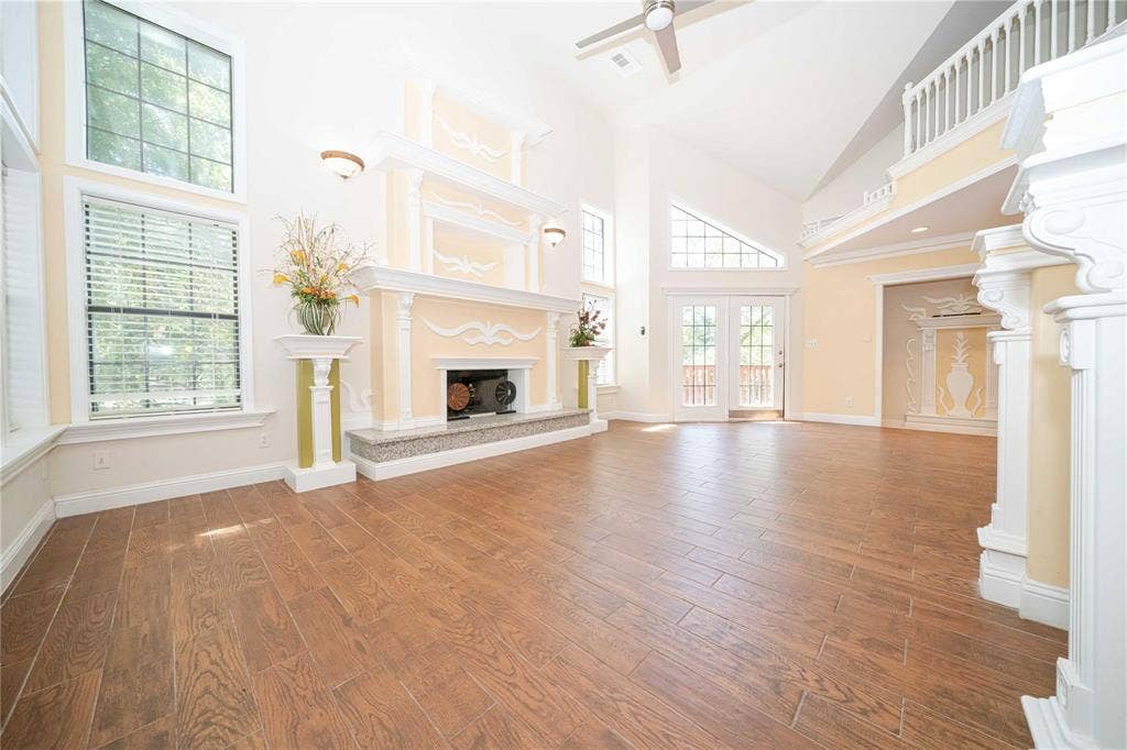 Vaulted ceilings with an upper-level mezzanine, wood-finish tile flooring, dual-story windows, and an ornate fireplace with a stone hearth