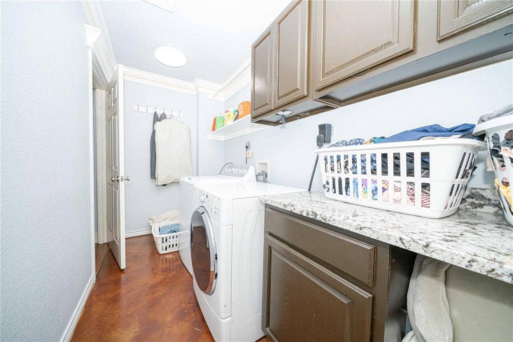 Utility room featuring stone-finish countertops, dark wood-finish cabinetry, crown molding, and stained concrete flooring