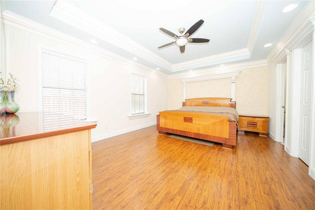 Tray ceiling with recessed lighting, central ceiling fan, wood-finish flooring, and crown molding