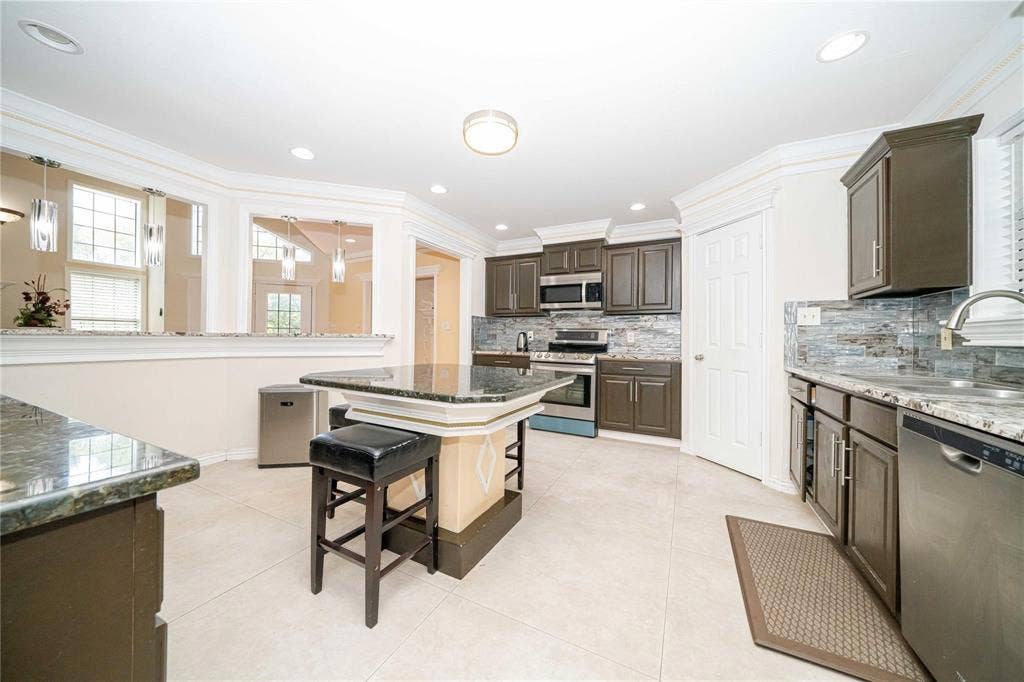 Kitchen featuring dark-finish cabinetry, stone countertops, central island, tiled flooring, and stainless steel appliances