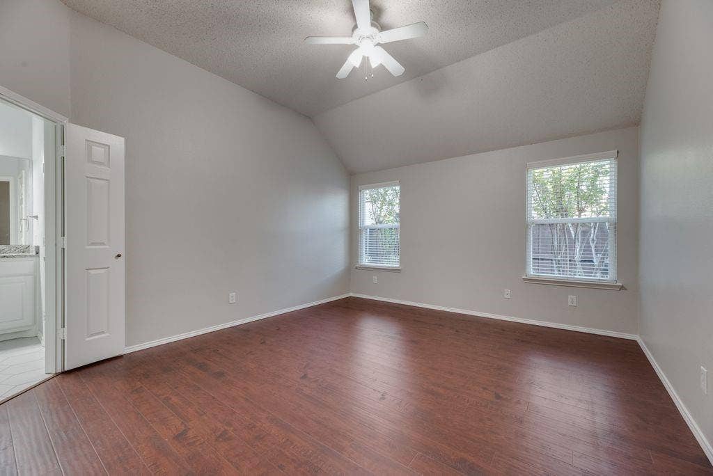 6310 Nueces Bay Drive, Rowlett, TX 75089 Spacious primary bedroom with wood floors, ceiling fan, raised ceiling, and ensuite bath.
