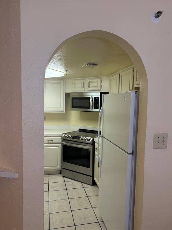 1010 Allen Street, #222, Dallas, TX 75204 Arched doorway leading to a kitchen featuring light cabinetry, tile flooring, and stainless steel appliances, including an over-the-range microwave and a slide-in range
