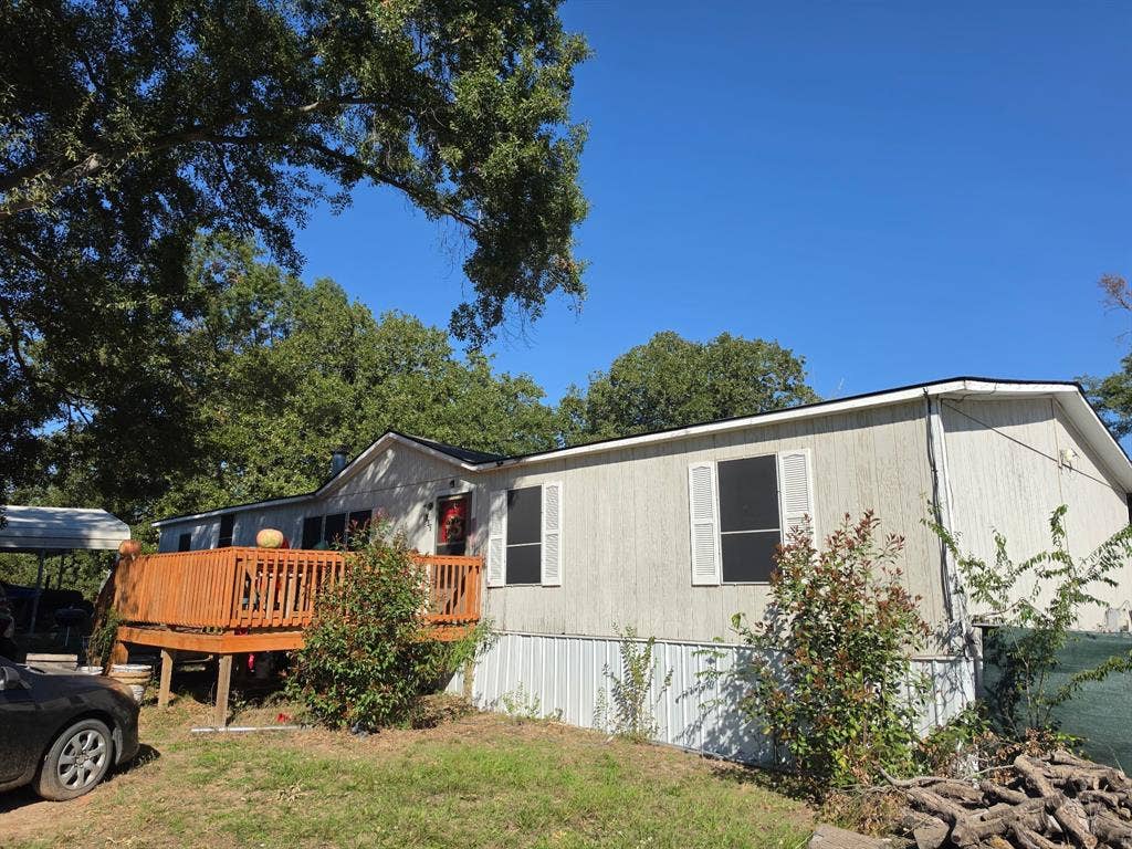 Exterior featuring a wood deck, vertical siding, shuttered windows, and a metal carport