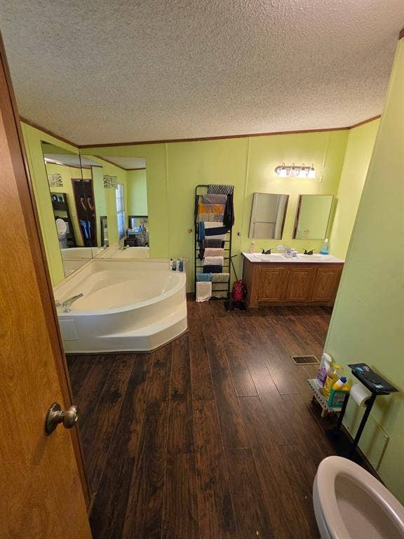 Bathroom featuring wood-finish flooring, a corner soaking tub, double-sink vanity with wood cabinetry, and wall-mounted vanity mirrors