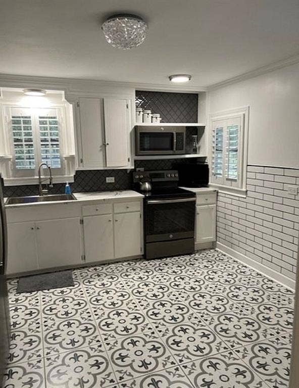 Kitchen featuring white cabinetry, subway tile wall accents, patterned tile flooring, integrated stainless steel appliances, and plantation shutters