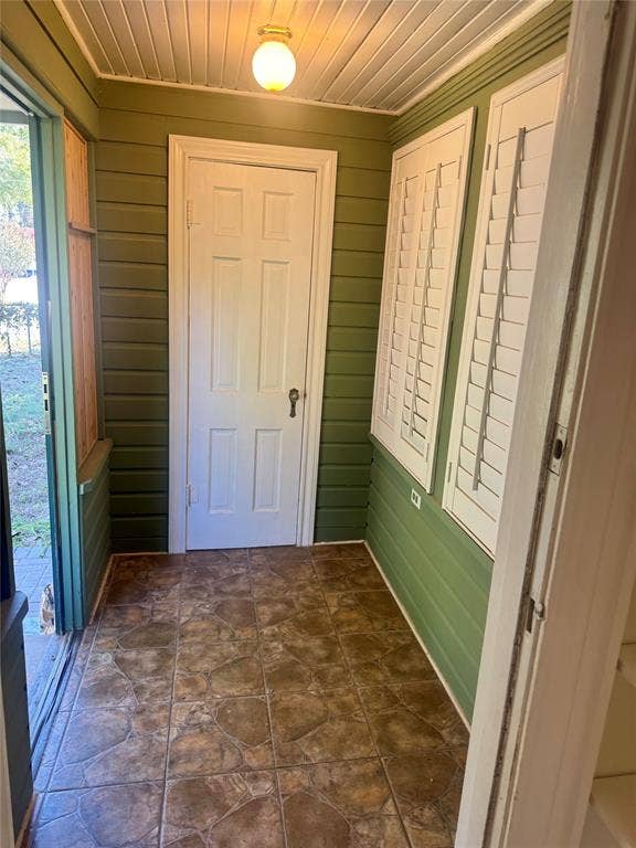 Covered porch featuring green horizontal siding, stone-patterned tile flooring, white shuttered windows, and a flush-mount ceiling light fixture