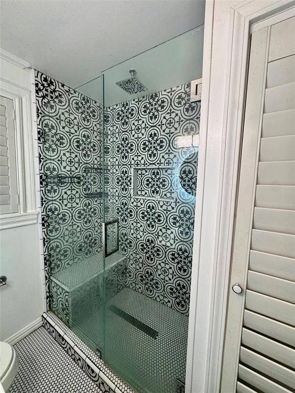 Walk-in shower featuring patterned tile walls, frameless glass enclosure, built-in tiled bench, rain-style shower head, and hexagonal floor tile