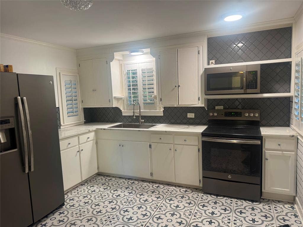 Kitchen featuring white shaker-style cabinetry, patterned tile flooring, dark-toned backsplash, stainless steel appliances, and a single-basin undermount sink