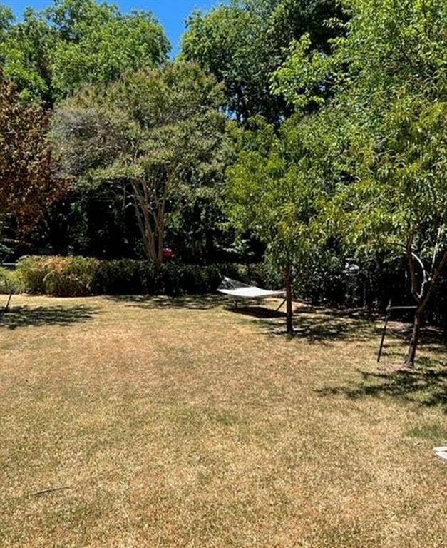 Expansive backyard featuring an open grass area, perimeter landscaping, and mature trees