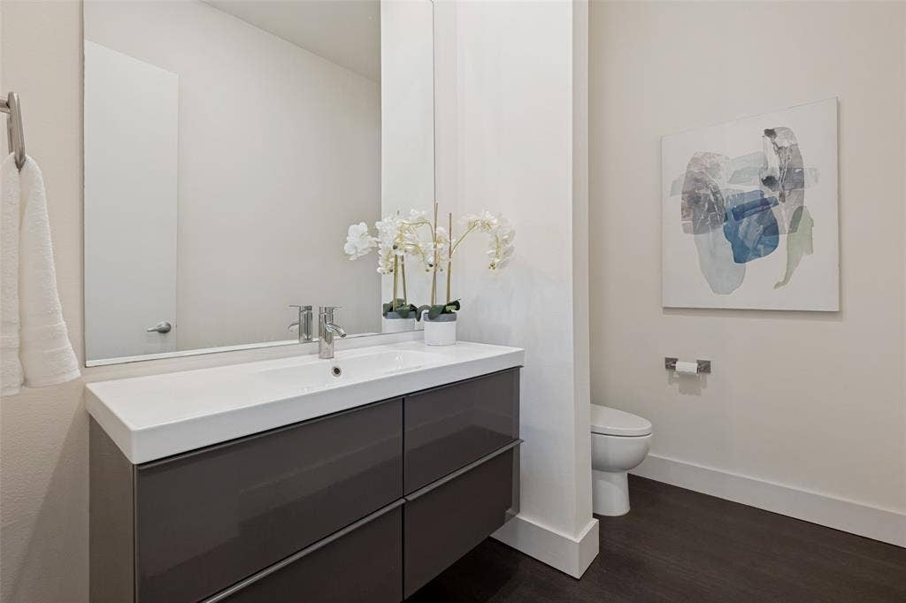 3336 Anchor Court, Dallas, TX 75219 Floating vanity featuring a high-gloss finish, white integrated rectangular sink, wall-spanning mirror, chrome-finish single-lever faucet, and wood-finish flooring