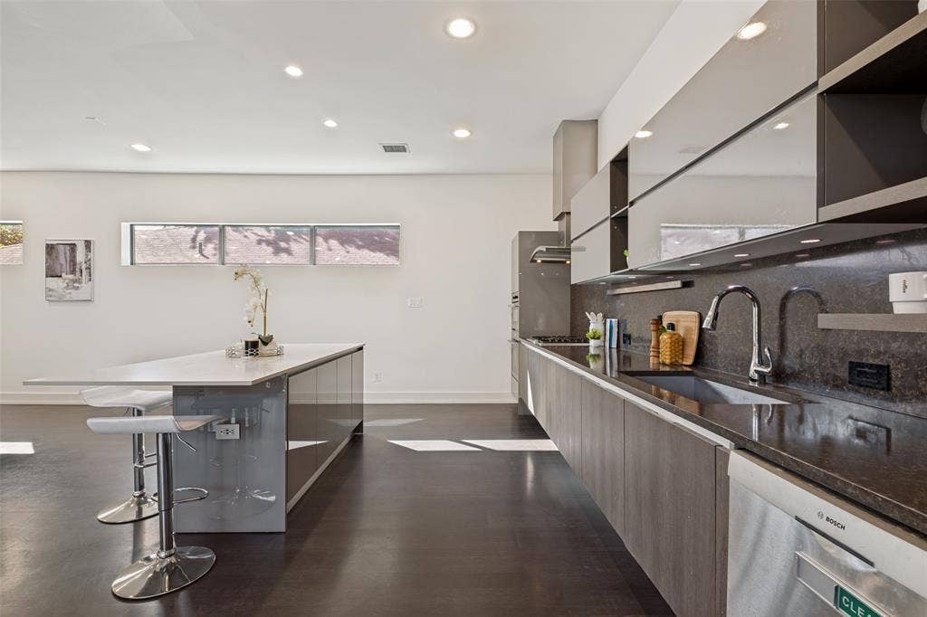 3336 Anchor Court, Dallas, TX 75219 Modern kitchen featuring high-gloss cabinetry, a central island with a quartz countertop, stone-surfaced backsplash, integrated stainless steel appliances, and recessed ceiling lighting