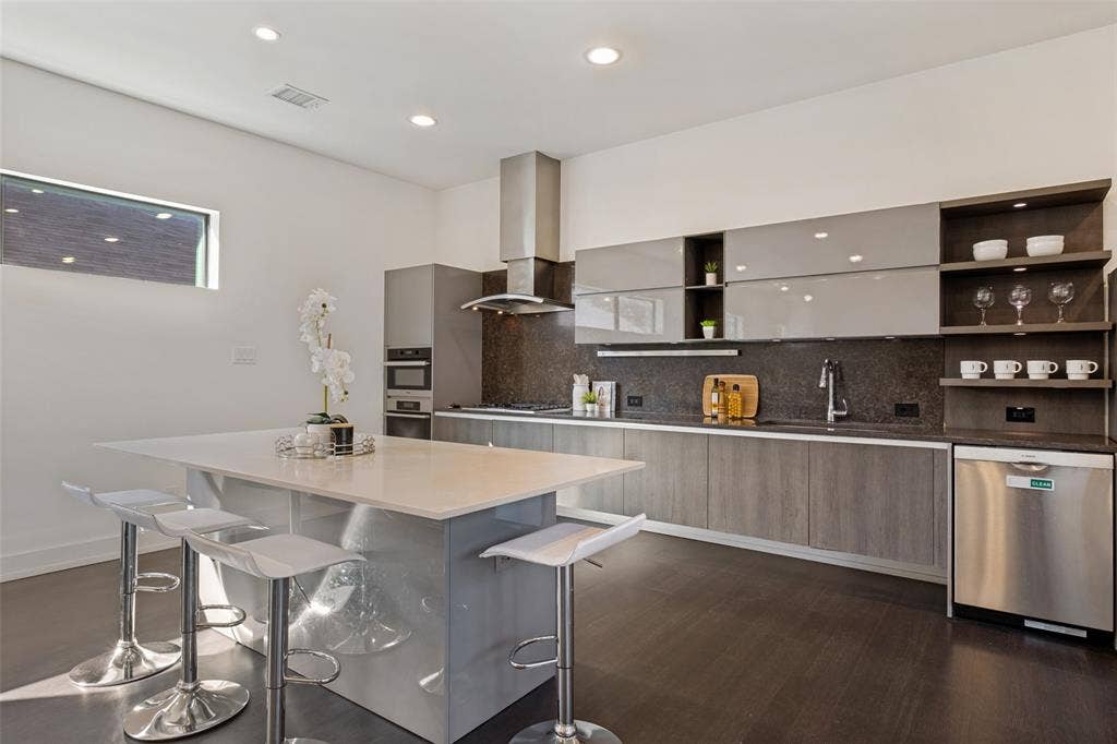 3336 Anchor Court, Dallas, TX 75219 Modern kitchen featuring high-gloss gray cabinetry, a central island with a solid-surface countertop, stainless steel appliances, open shelving, and dark-toned wood-finish flooring