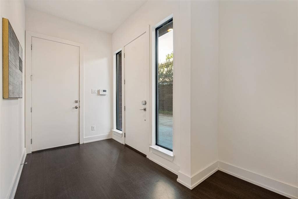 3336 Anchor Court, Dallas, TX 75219 Entry area featuring dark wood-finish flooring, crisp white walls, vertical fixed-pane windows with black frames, and solid-core interior doors with satin nickel hardware