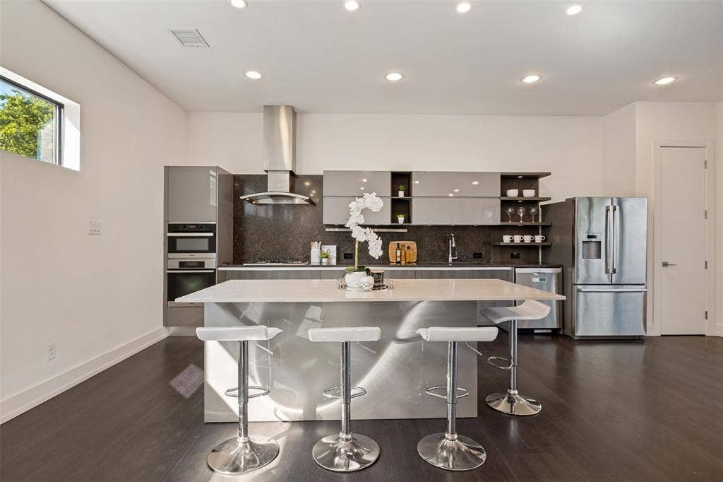 3336 Anchor Court, Dallas, TX 75219 Contemporary kitchen featuring high-gloss cabinetry, a central island with a solid-surface countertop, stainless steel appliances, and dark wood-finish flooring