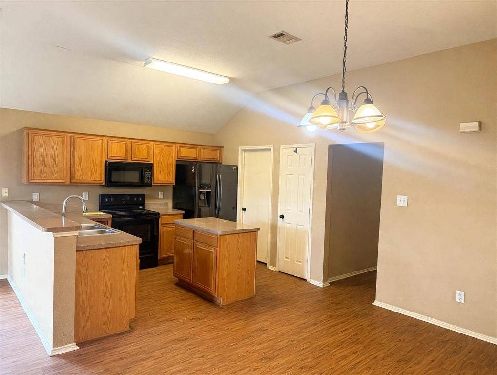 2053 Wild Creek Court, Dallas, TX 75253 Kitchen featuring wood-finish cabinetry, a central island with a solid-surface countertop, wood-finish flooring, and vaulted ceilings