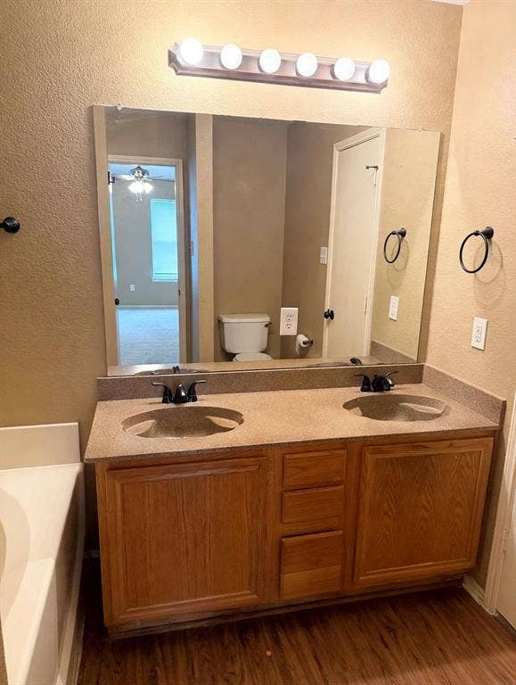 2053 Wild Creek Court, Dallas, TX 75253 Dual-basin vanity featuring a stone-composite countertop, warm-toned wood cabinetry, matte black dual-handle faucets, and a full-width mirror with overhead light fixture