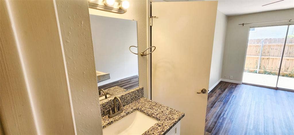 4402 Tophill Lane, Irving, TX 75038 Bathroom vanity featuring a stone-composite countertop, undermount sink, and polished metal faucet with integrated mirror and overhead light fixture