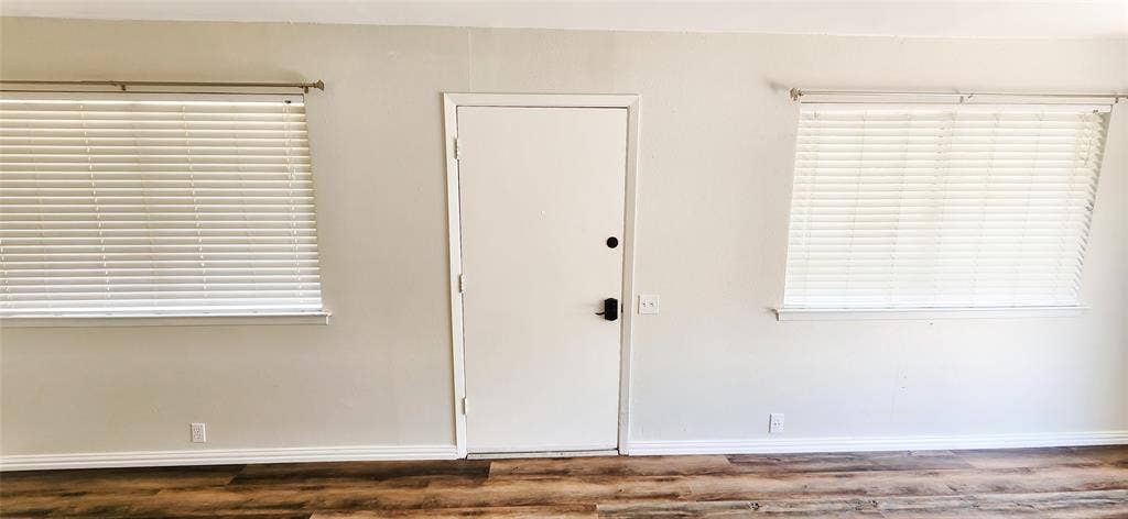 4402 Tophill Lane, Irving, TX 75038 Interior wall featuring wood-finish flooring, two large windows with horizontal blinds, and a central entry door with an electronic deadbolt