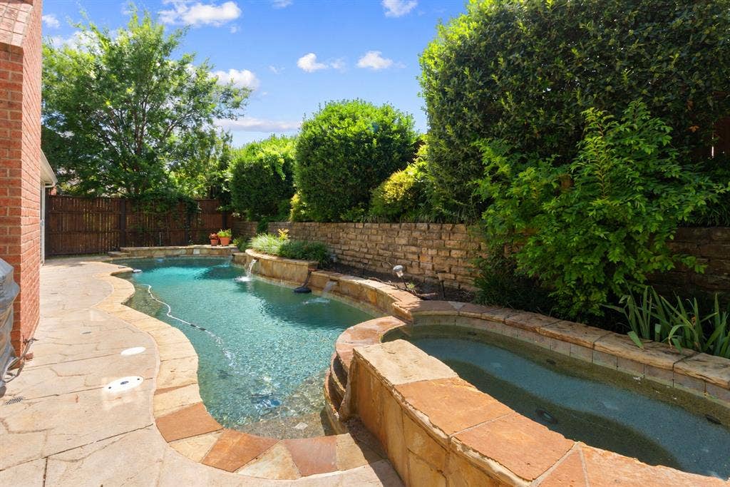 1110 Wedge Hill Road, McKinney, TX 75072 Freeform swimming pool featuring flagstone coping, an integrated spa, and stacked stone water features set within a fenced backyard