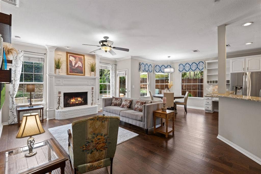 1110 Wedge Hill Road, McKinney, TX 75072 Open-concept interior featuring wood-finish flooring, a white brick fireplace with a decorative mantel, recessed lighting, and a kitchen peninsula with stone-finish countertops