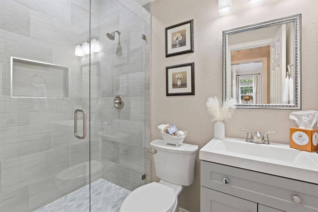 1110 Wedge Hill Road, McKinney, TX 75072 Walk-in shower with floor-to-ceiling ceramic tile, glass enclosure, and built-in recessed niche; vanity featuring a rectangular integrated sink and cabinet storage; wall-mounted vanity mirror