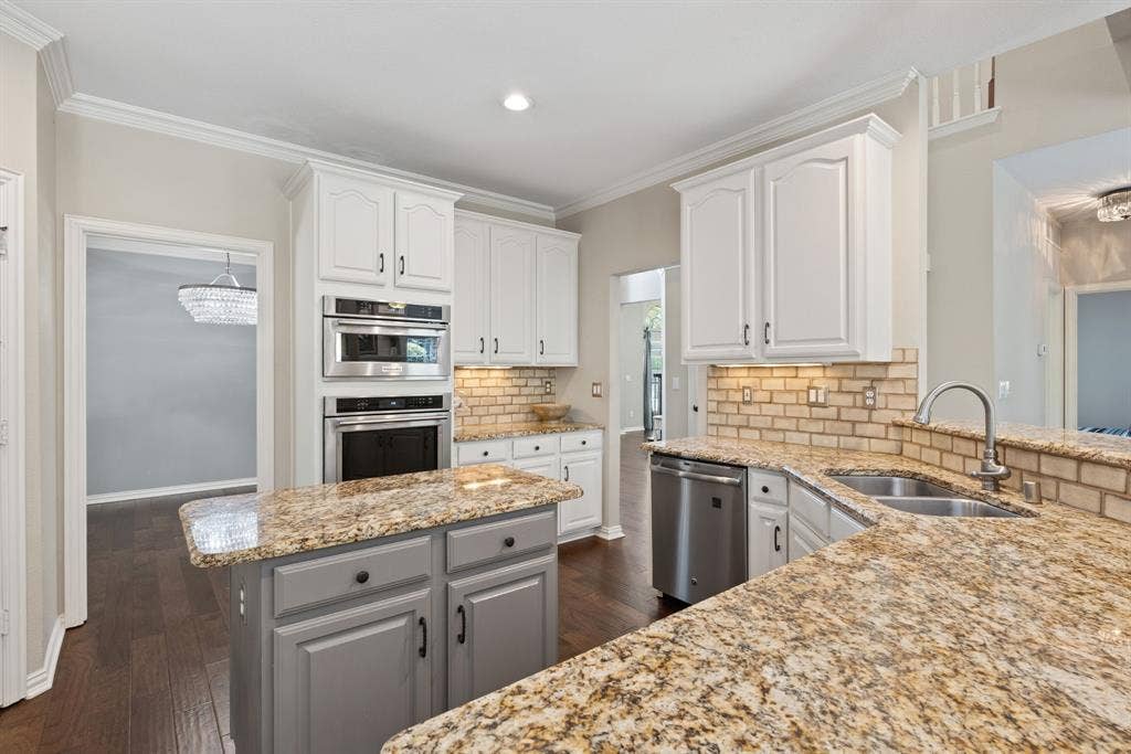 1110 Wedge Hill Road, McKinney, TX 75072 Kitchen featuring stone countertops, white upper cabinetry, a grey center island, stainless steel built-in double ovens, and a brick-pattern backsplash