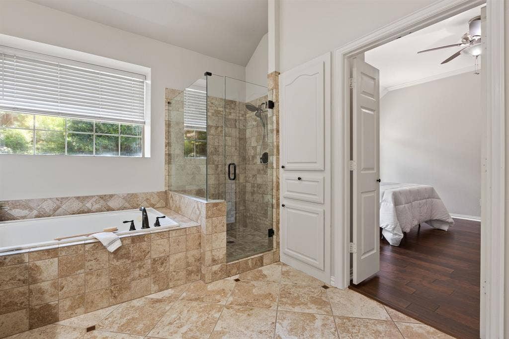 1110 Wedge Hill Road, McKinney, TX 75072 Bathroom featuring a drop-in soaking tub and glass-enclosed shower with tiled surround, stone-finish tile flooring, and custom cabinetry with matte black hardware