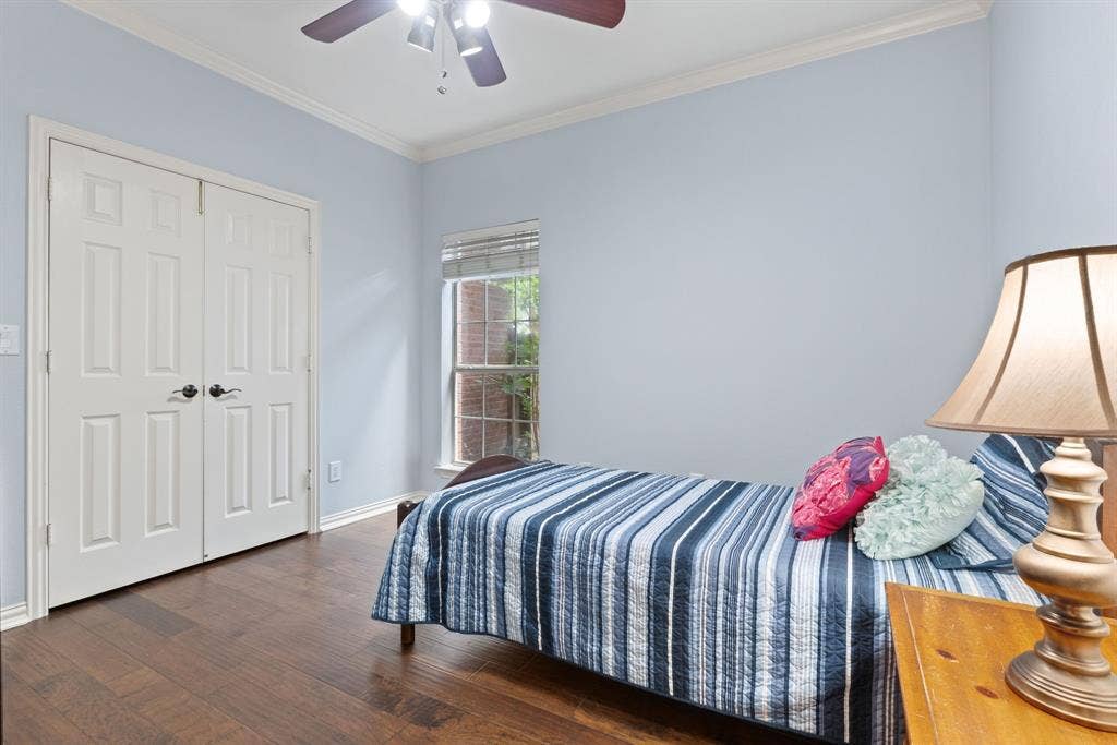 1110 Wedge Hill Road, McKinney, TX 75072 Wood-finish flooring, double-door closet with dark hardware, crown molding, and ceiling fan with integrated lighting
