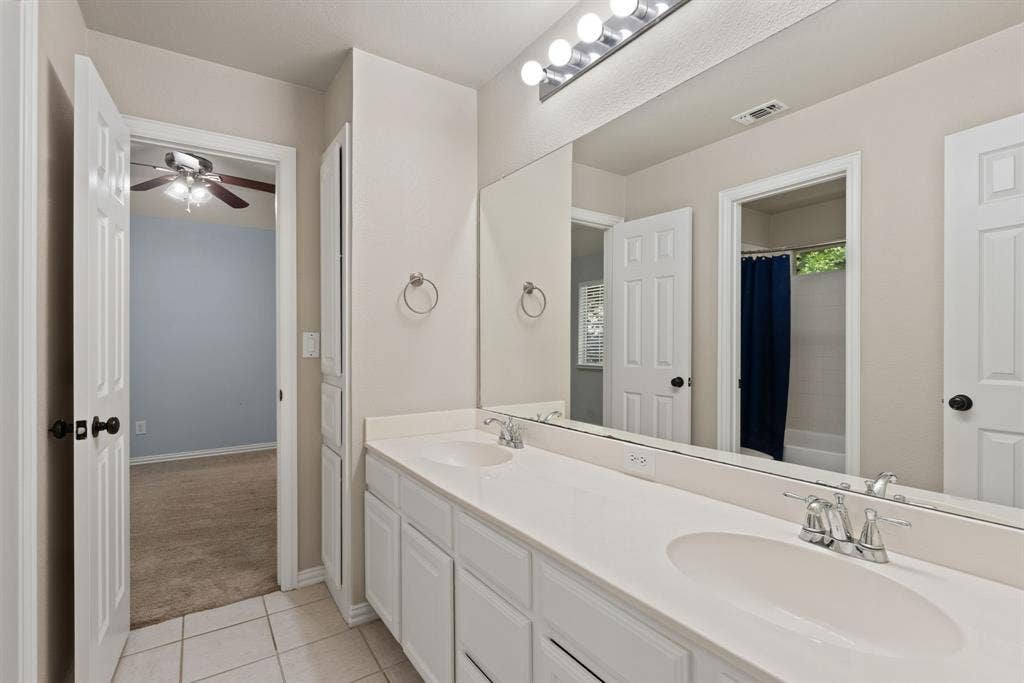 1110 Wedge Hill Road, McKinney, TX 75072 Double vanity featuring dual integrated sinks, white cabinetry, a full-width mirror, and a multi-bulb light fixture