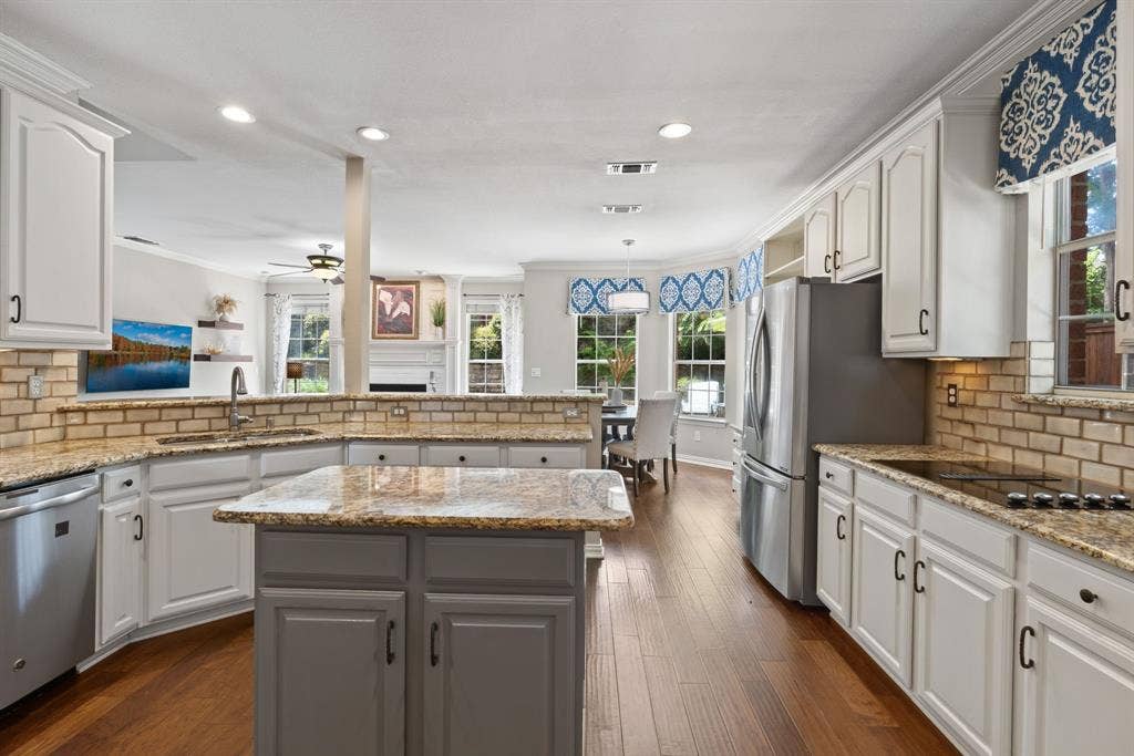 1110 Wedge Hill Road, McKinney, TX 75072 Kitchen featuring custom white cabinetry, stone countertops, brick-style tile backsplash, wood-finish flooring, and a central island with a contrasting finish