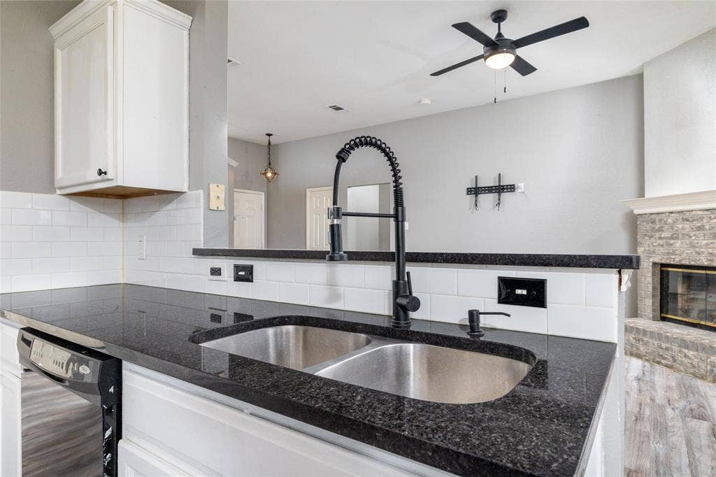 224 Cobblestone Circle, Red Oak, TX 75154 Kitchen featuring dark stone countertops, white subway tile backsplash, stainless steel dual-basin sink, matte black gooseneck faucet, and white cabinetry