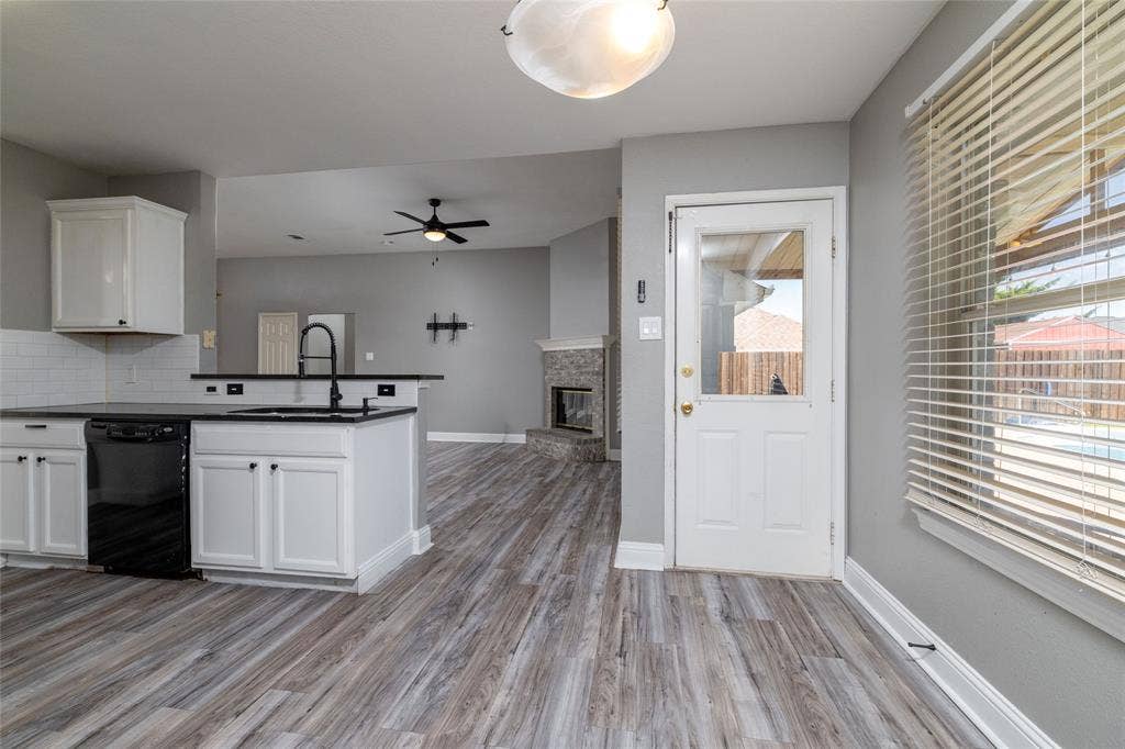 224 Cobblestone Circle, Red Oak, TX 75154 Kitchen featuring white cabinetry, dark countertops, a black pull-down faucet, wood-finish flooring, and a stone-surround fireplace