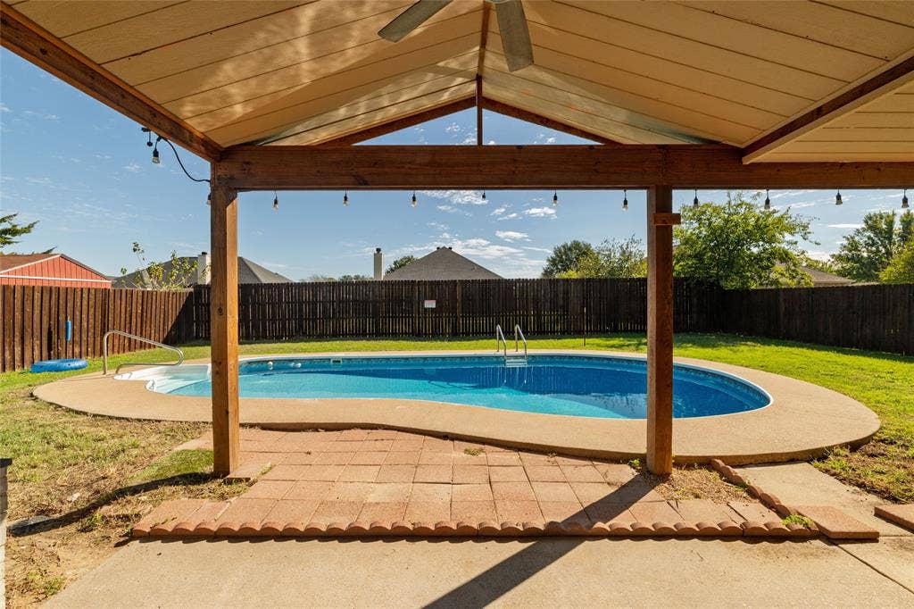 224 Cobblestone Circle, Red Oak, TX 75154 Covered patio with wood-beam construction, ceiling fan, and string lighting, featuring a backyard pool with concrete surround and full wood fencing