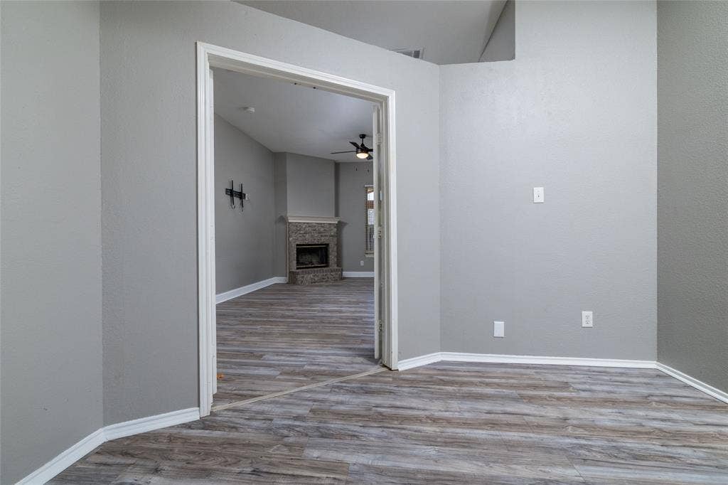 224 Cobblestone Circle, Red Oak, TX 75154 Interior room featuring wood-finish flooring, neutral wall tones, and a doorway leading to a space with a floor-to-ceiling stone fireplace and a ceiling fan