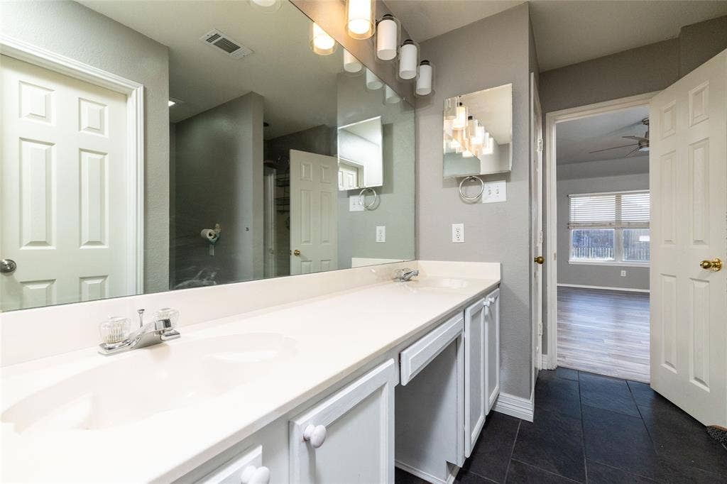 224 Cobblestone Circle, Red Oak, TX 75154 Dual-sink vanity with a solid-surface countertop, full-width wall mirror, five-light fixture, and dark-toned flooring