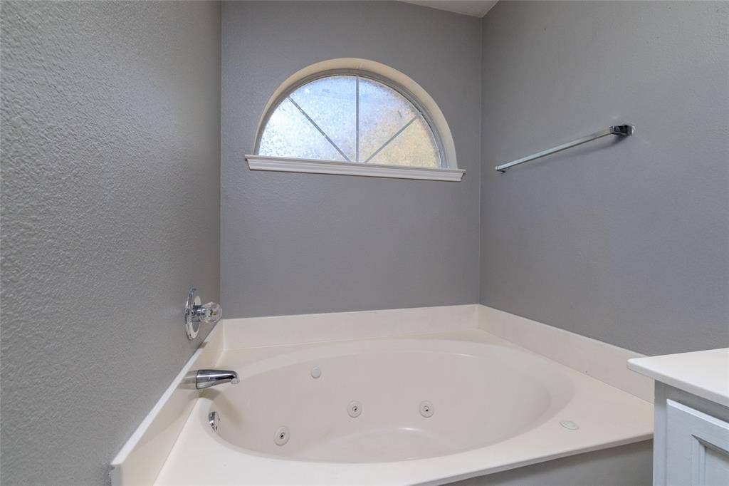 224 Cobblestone Circle, Red Oak, TX 75154 Oval jetted soaking tub with a solid-surface deck, arched window with a fanlight design, and a metallic wall-mounted towel bar