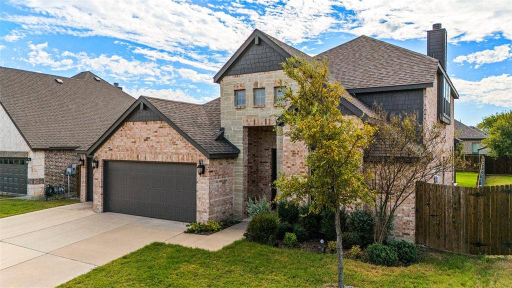 408 Abbott Lane, Waxahachie, TX 75165 Two-story exterior featuring a brick and stone facade, dark shingle roof, integrated two-car garage, and cedar privacy fencing
