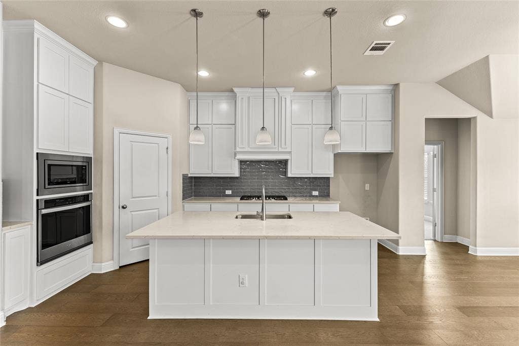 408 Abbott Lane, Waxahachie, TX 75165 Kitchen featuring a large central island with light-toned solid surface countertops, white shaker-style cabinetry, a dark tiled backsplash, stainless steel built-in double ovens, and three pendant light fixtures over the island