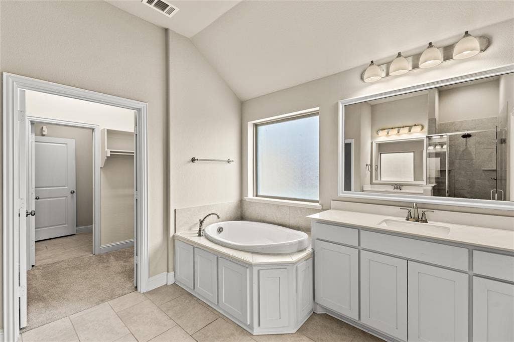 408 Abbott Lane, Waxahachie, TX 75165 Bathroom featuring a drop-in soaking tub with a tiled surround, a large framed vanity mirror, white cabinetry with a light-toned countertop, and recessed lighting